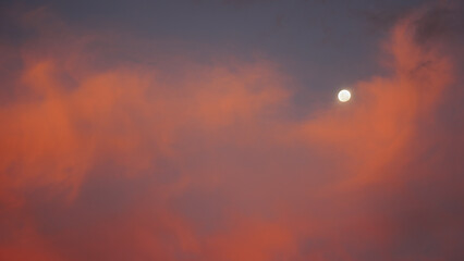 The moon set behind colorful red clouds at sunset
