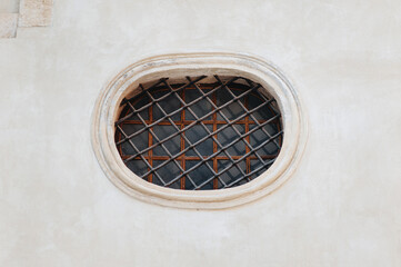 Antique old round, oval window with dark iron bars framed on a gray wall. The Armenian church in Lviv.