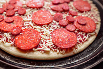 Simple uncooked pepperoni pizza on a metal round cooking tray. Close up. Selective focus. Italian world known dish with dough, cheese and meat and sauce.