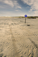 Car tire tracks on a beach and direction sign. Omey island, county Galway, Ireland. low tide....