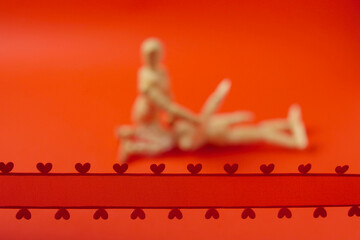 Red ribbon with hearts in focus. Couple making love out of focus. Juicy red background. Adult...