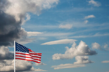 Waving bright flag of United States of America against blue cloudy sky. One cloud mimics shape of...