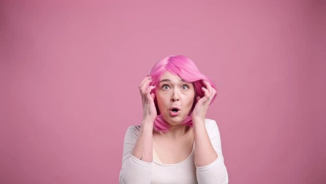 Portrait of shocked woman on pink background. Young female in pink wig has her head boiled.