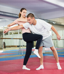 Fototapeta na wymiar Concentrated girl performing knee kick with wrist lock to male opponent while sparring during self defense training in gym