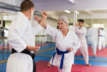 Portrait of mature woman wearing white kimono sparring with male opponent during martial arts training © JackF
