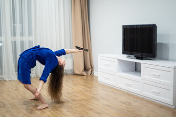 flexible woman exercising at home in front of tv screen, stretching her back. Concept of individuality, creativity and self-confidence
