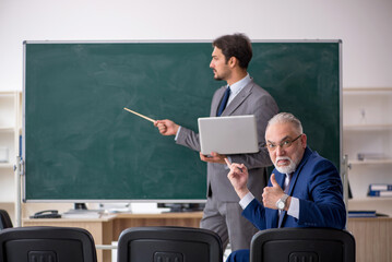 Young male employee and old boss in front of blackboard