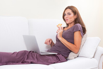 young girl with a laptop and eating a sweet, smiling at the camera with complicity
