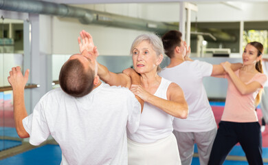 Determined aged woman practicing effective self defence techniques with male sparring partner in...