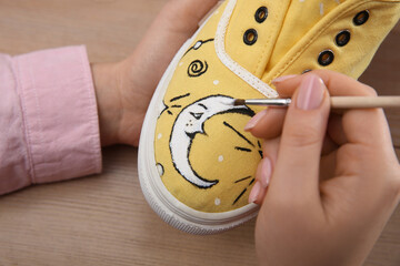 Woman painting on sneaker at wooden table, closeup. Customized shoes