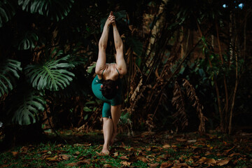 Beautiful woman green body in a green forest doing yoga and ballet exercise pose. Brown woods with leaves