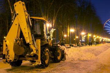 cleaning snow in the park in winter with a tractor in the evening