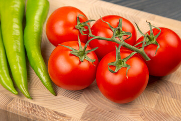 red tomatoes and green hot peppers on a kitchen board