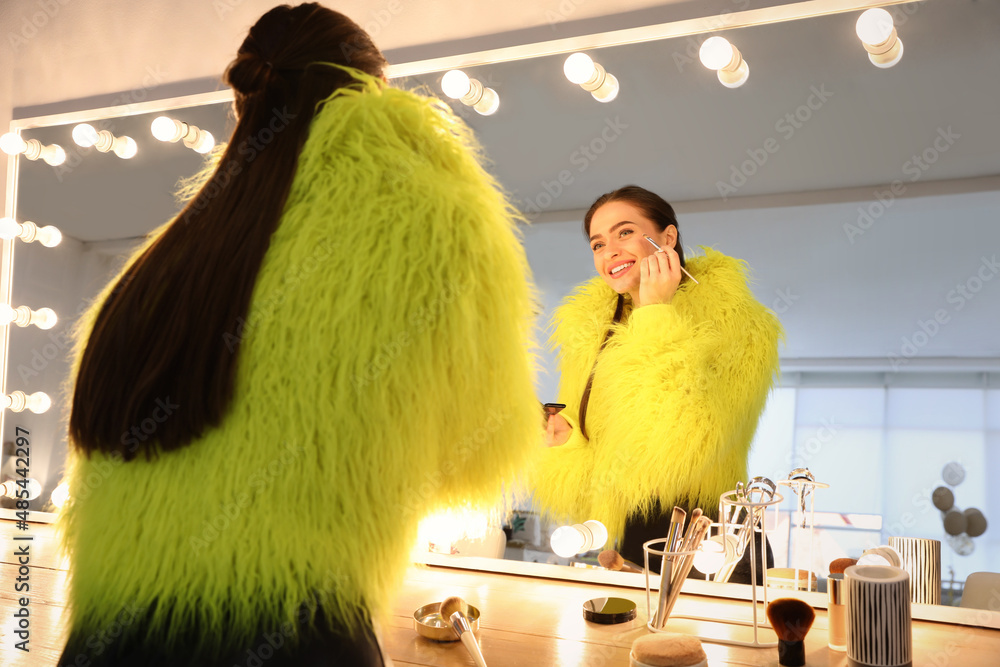 Wall mural Young woman applying make up near illuminated mirror indoors