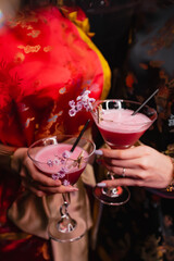 Girls in kimano are holding two red cocktails decorated with pink flowers. Party concept, night club