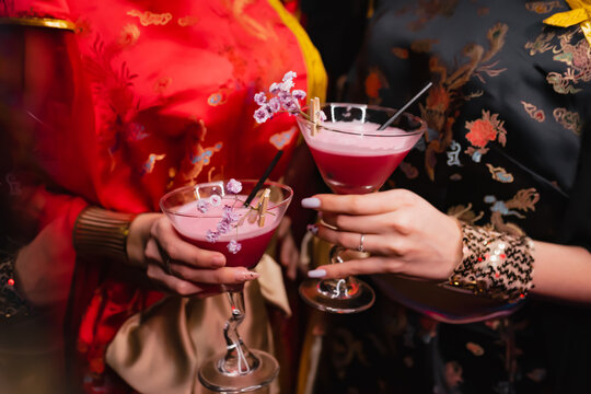 Girls in kimano are holding two red cocktails decorated with pink flowers. Party concept, night club