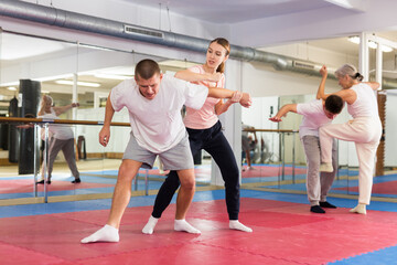 Fototapeta na wymiar Caucasian woman performing elbow strike while sparring with man in gym during self-defence training. Senior woman training in background.