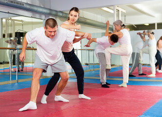 Obraz premium Caucasian woman performing elbow strike while sparring with man in gym during self-defence training. Senior woman training in background.