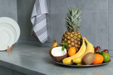 Plate with different ripe fruits on grey countertop. Space for text