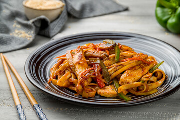 Udon noodles with chicken and vegetables on grey wooden table macro close up