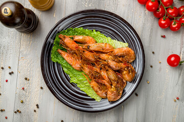 Roasted shrimps with lemon and greens on plate on grey wooden table top view