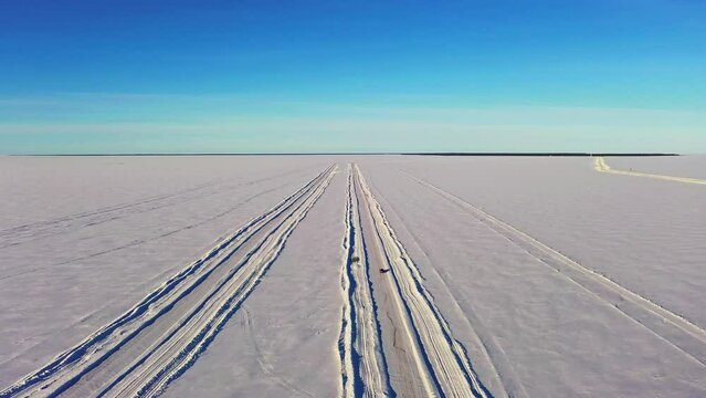 Aerial drone view following a vehicle on a winter road, car crossing frozen ocean ice