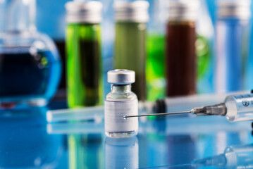 vial with Covid-19 vaccine and a syringe with a drop of vaccine on the needle.