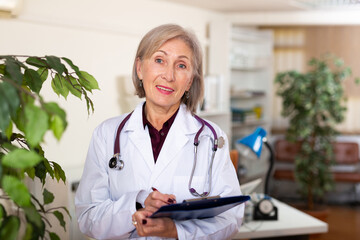 Portrait of confident mature woman doctor standing at clinic office