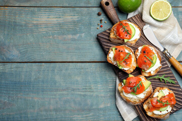 Delicious sandwiches with cream cheese, salmon, avocado and arugula served on light blue wooden table, flat lay. Space for text