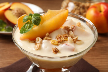 Tasty peach yogurt with granola, mint and pieces of fruit in dessert bowl on table, closeup