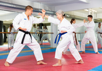 Portrait of mature woman wearing white kimono sparring with male opponent during martial arts...