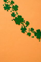 Happy St. Patrick's Day composition. Green shamrock clover leaves on orange background. Flat lay, top view.
