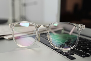 Fototapeta na wymiar Glasses and newspapers on modern laptop, closeup