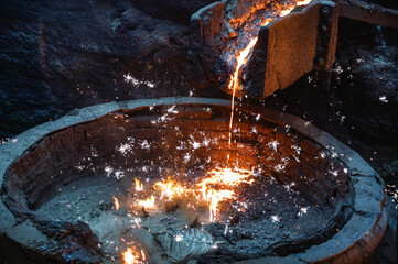 Liquid cast iron is poured into the ladle in a thin stream. Lots of sparks.