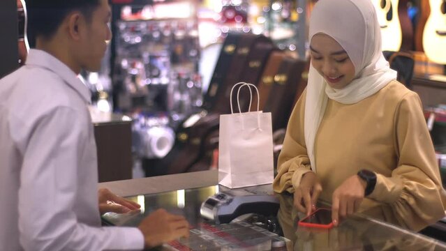 An upwardly mobile Asian Muslim woman using a smartwatch to pay for a product at a sale terminal with nfc identification payment for verification and authentication