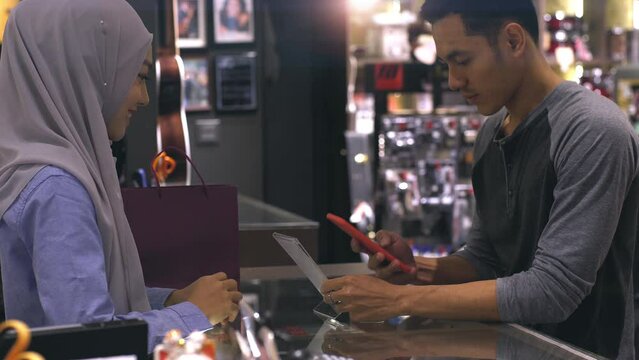 An upwardly mobile Asian Muslim man using a mobile phone to scan the QR Code to pay for a product at a sale terminal identification payment for verification and authentication