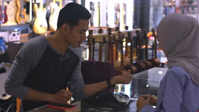 An upwardly mobile Asian Muslim man using a smartwatch to pay for a product at a sale terminal with nfc identification payment for verification and authentication