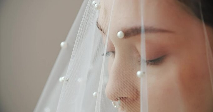 Close-up portrait gorgeous young woman seductively looks outside the window. Stylish wedding photo session of charming sensual bride under white veil. Beautiful make-up girl's face. Bridal day concept