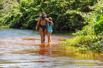 Mãe e filha caminhando dentro agua do rio