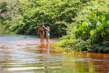 Mãe e filha caminhando dentro agua do rio