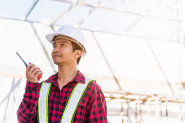 Asian engineer foreman architect worker man working at building construction site talking with radio, engineering hold radio discuss operate and control worker employee to building construction