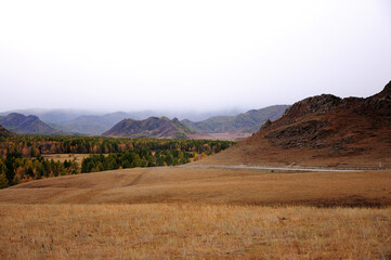 Fototapeta na wymiar An asphalt road skirting a high hill goes through a dry autumn steppe under thunderclouds.