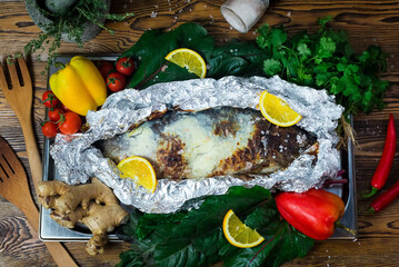 Baked whole fish in foil. The fish is sprinkled with coarse salt. Surrounded with bell peppers,...