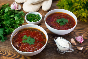Two deep plates of borscht. Traditional Russian-Ukrainian beet soup. Traditional dish of the Eastern Slavs, the main first course. Served with sour cream, parsley and garlic.