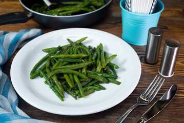 Green beans steamed, drizzled with oil and salt. White plate with a portion of cooked beans. Healthy eating and calorie control. Ideal for vegetarians.