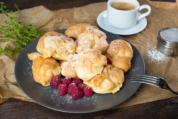 A pile of profiteroles sprinkled with powdered sugar. Served with fresh raspberries and coffee.