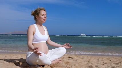 Fototapeta na wymiar Tranquil stunning pregnant woman meditating and suntanning on the sandy ocean beach, lotus yoga pose