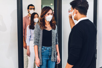 Group of professional asian business and using infrared thermometer for checking body temperature staff fever before work in quarantine for coronavirus wearing protective mask at office
