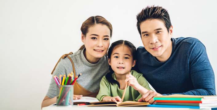 Portrait enjoy happy love asian family father and mother with asian girl learn and study on table.Mom and dad with asian young girl writing with book make homework in homeschool at home.Education