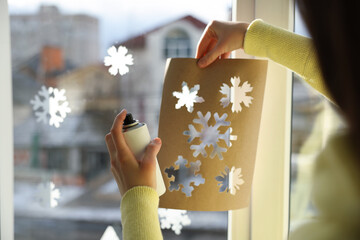 Woman using snow spray for decorating window with snowflakes at home, closeup